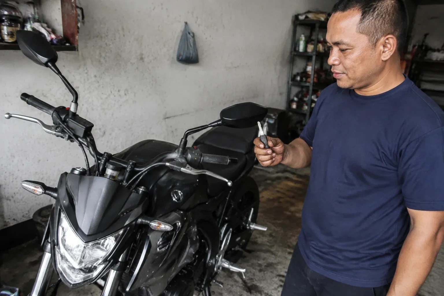 Person holding a key beside a black motorcycle in a garage. — Motorcycle & Scooter Keys, Brampton